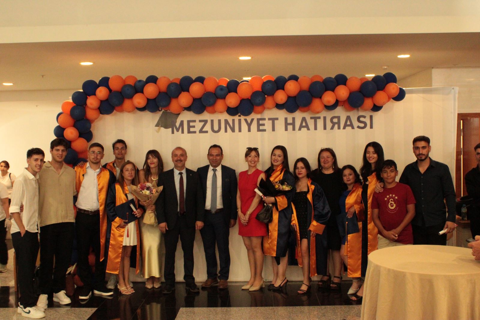 Mezun olan öğrenciler ve öğretim elemanları mezuniyet hatırası tabelası önünde fotoğraf çektiriyor.